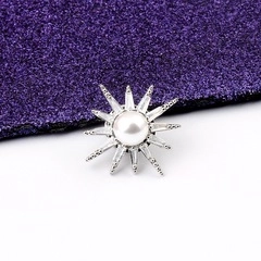 Macro detail of sunburst star brooch featuring center pearl and zircon rays
