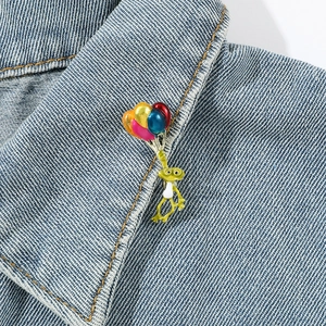 Détail du pin's émaillé grenouille avec ballons colorés sur un col de veste en jean