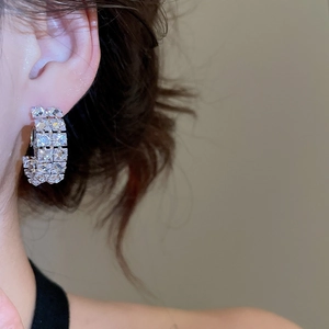 Close-up of C-shaped silver earrings with sparkling double-row square zircon stones