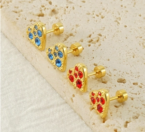 Macro di orecchini a cuore dorati con pietre blu e rosse su sfondo in pietra beige