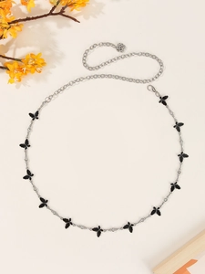 Detailed close-up of a silver butterfly waist chain with black accents on beige background