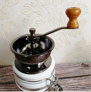 Detail of manual coffee grinder with wooden handle, metal burr, and white ceramic jar