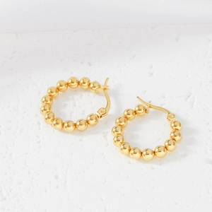 Close-up of polished gold beaded geometric earrings on a white textured background