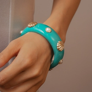 Détail d'une manchette en résine turquoise avec coquillages dorés et perles au poignet