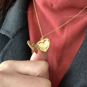 Locket necklace with heart-shaped gold pendant shown on model with a red background