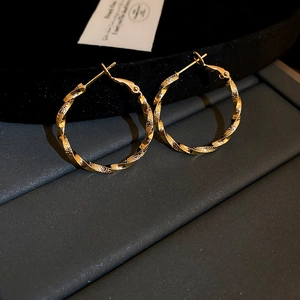 Macro detail of gold-plated twisted hoop earrings on a black velvet display