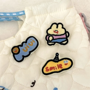 Close-up of cute cartoon rabbit embroidery patches and smile pins on white quilted bag