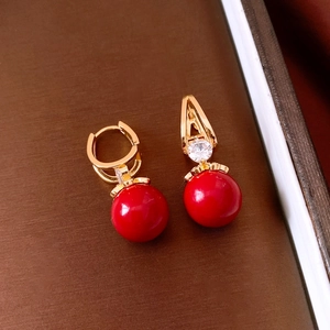 Detailed close-up of retro gold earrings with red resin beads and sparkling zircon accents