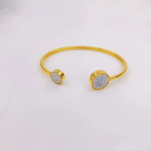 Detail of gold open cuff bracelet featuring two round ends encrusted with white crystals
