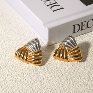 Macro view of two-tone gold and silver fan-shaped earrings on a beige textured surface