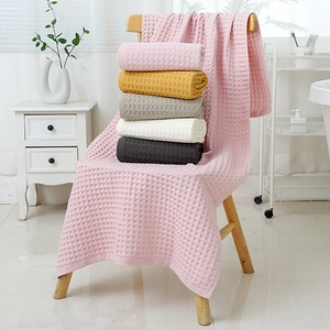 Pink waffle weave cotton bath towel set displayed on a wooden chair in a bright home setting