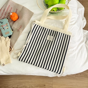 Detailansicht eines gestreiften Kordelzug-Rucksacks mit Retro-Label auf weißem Bett