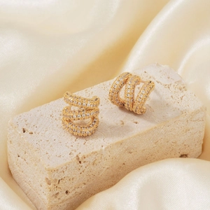 Luxuriöse goldene C-förmige Creolen mit Zirkonia-Mikropavé auf elegantem Seidenhintergrund