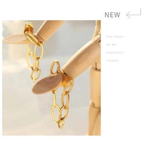 Detail of gold chain link earrings draped on a wooden hand model for a modern look