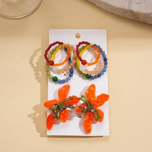 Colorful resin bead geometric hoops and orange acrylic flower earrings set on a white card