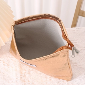 Detail view of the gold makeup bag open to show the grey interior lining and metal texture