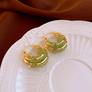 Detail shot of golden zircon earrings with green enamel on a ceramic plate