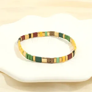 Macro detail of colorful Tila bead tile bracelet with gold accents on white tray