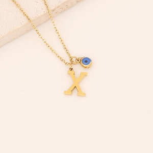 Détail macro du pendentif lettre X doré et de l'œil bleu sur une chaîne épurée