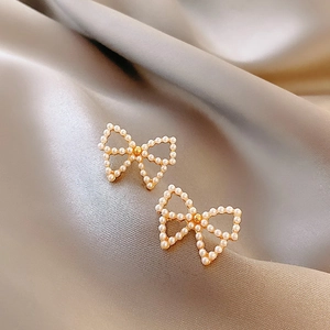 Close-up of pearl bow stud earring on champagne silk background with soft lighting
