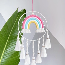 Detail of bohemian woven rainbow wall hanging with pink blue tassels and white poms