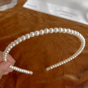 Close-up of elegant white faux pearl headband held against brown velvet background