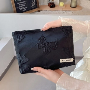 Detail of black fabric toiletry bag with embossed bow patterns and white side label