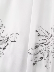 Close-up of intricate beaded embroidery on smooth white fabric for a luxury women shirt
