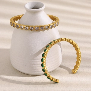 Dettaglio di bracciali in zircone a cuore placcati oro 18K su un vaso bianco minimalista
