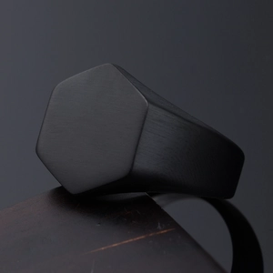 Detail of matte black hexagonal signet ring with brushed finish on dark wooden stand