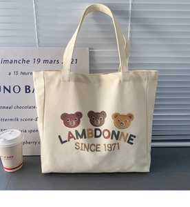 Close-up of the colorful teddy bear embroidery on a cream canvas tote bag detail