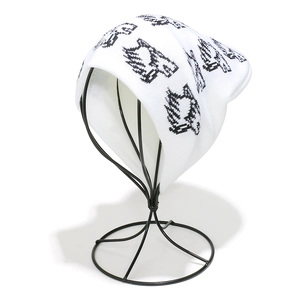 Close-up of white knitted beanie with black pixel patterns on a display stand