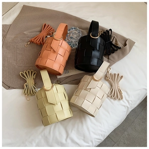 Detail view of woven bucket bags in orange, black, yellow, and cream with metal handles