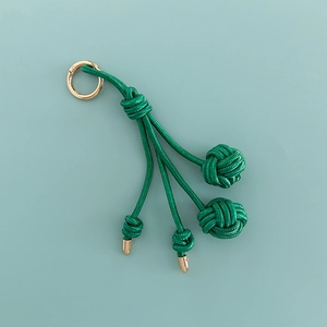 Dettaglio del ciondolo borsa intrecciato verde con anello dorato e nodi fatti a mano