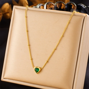 Close-up of a golden heart necklace with emerald gemstone on a satin display stand