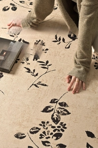 Detailed texture of beige plush carpet with black floral patterns in warm sunlight