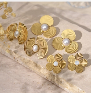 Détail de boucles d'oreilles dorées avec perles et nacre sur pierre beige