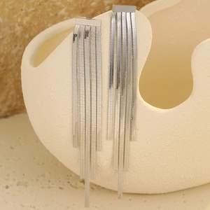 Close-up of silver long tassel earrings hanging on a beige organic ceramic vase