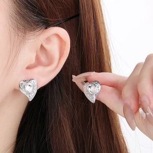 Dettaglio macro di orecchini a cuore testurizzati con strass brillanti sulla modella