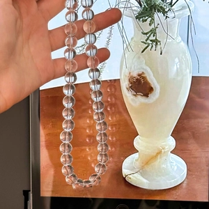 Detailed close-up of a clear crystal bead necklace held against a decorative background