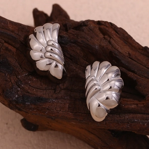 Macro detail of silver half-circle wave flower stud earrings on dark textured wood background