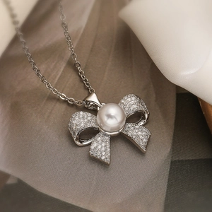 Elegant silver finish bow necklace with zircons and large white pearl on silk fabric