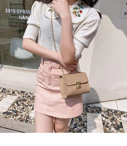 Close-up of a small plaid crossbody bag with gold chain strap on a white knit top