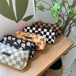 Corduroy pencil cases with checkerboard and floral patterns arranged on a wooden desk