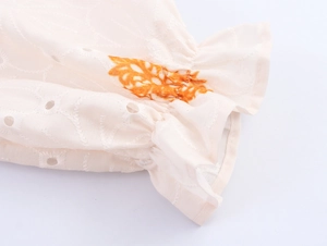 Detalle de puños elásticos con volantes y bordados florales en un vestido beige de lino