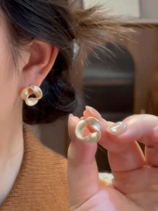 Close-up of 14K gold plated knot earrings with textured edges on model