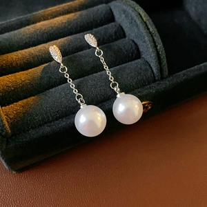 Detailed view of silver drop earrings with white pearls and crystals on black velvet