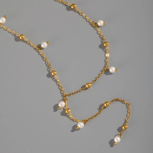 Dettaglio di un'elegante collana di perle dorate con pendenti di perle bianche su sfondo grigio