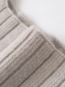 Macro detail of the light taupe rib-knit fabric texture with soft premium wool fibers