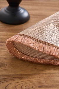 Detail of rose gold woven placemat with metallic fringe on dark wood table